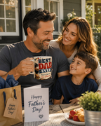 A man and woman, presumably a father and son, are sitting together at a table, smiling and enjoying each other's company. The man is holding a mug with a humorous text on it, and there is a card that reads "Happy Father's Day!" in front of them.