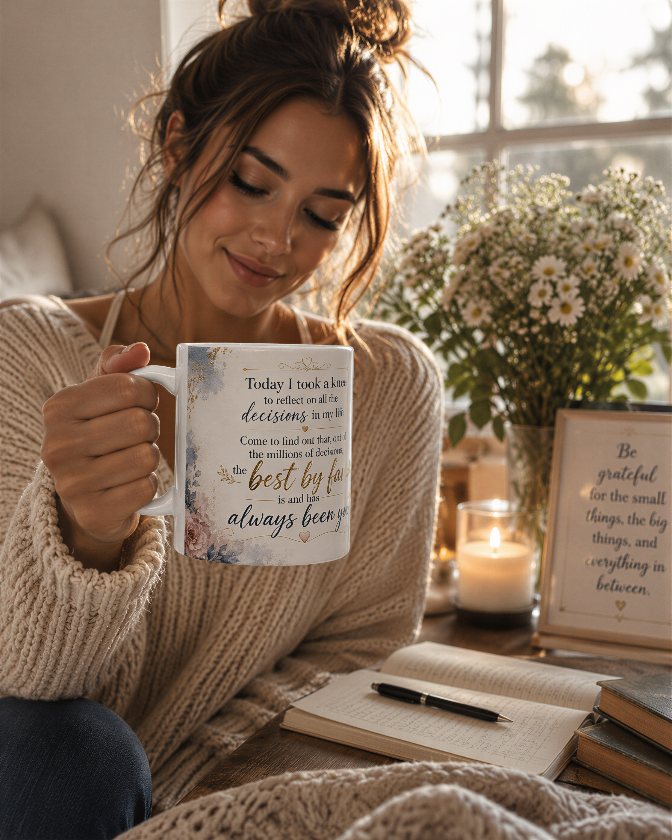 A woman sits on a couch, holding a mug with a quote, while a vase of flowers and a candle are nearby.