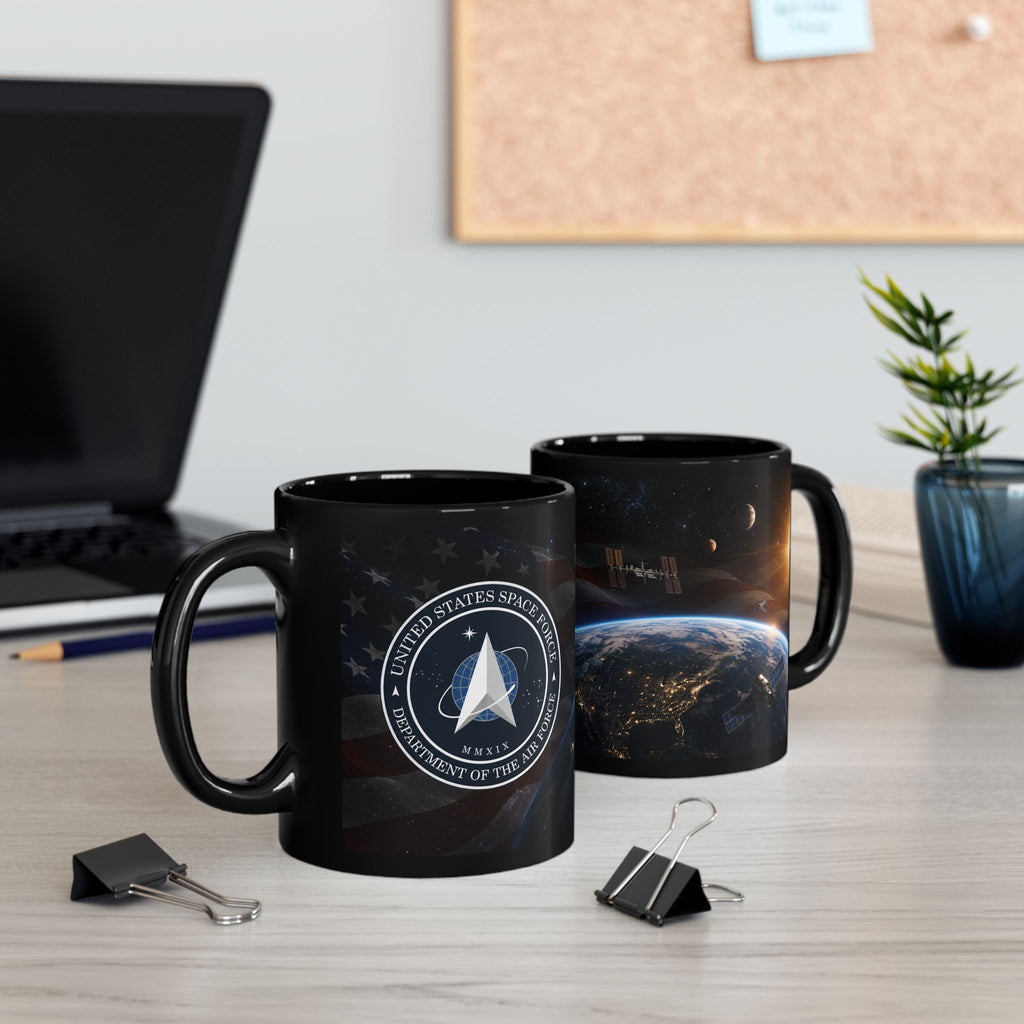 two black mugs with space-themed designs, placed on a desk with a laptop, a plant, and some office supplies.