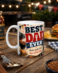 A white mug with a design featuring a barbecue grill and the text "BEST DAD EVER Master of the Grill. Hero of the Chill" is placed on a wooden table.