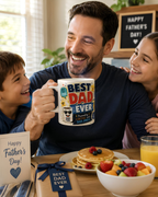 A man is holding a mug with the text "BEST DAD EVER" while sitting at a table with two children and a plate of pancakes.
