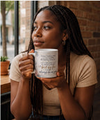 A woman with braided hair is holding a mug with text on it, looking to the side with a thoughtful expression.