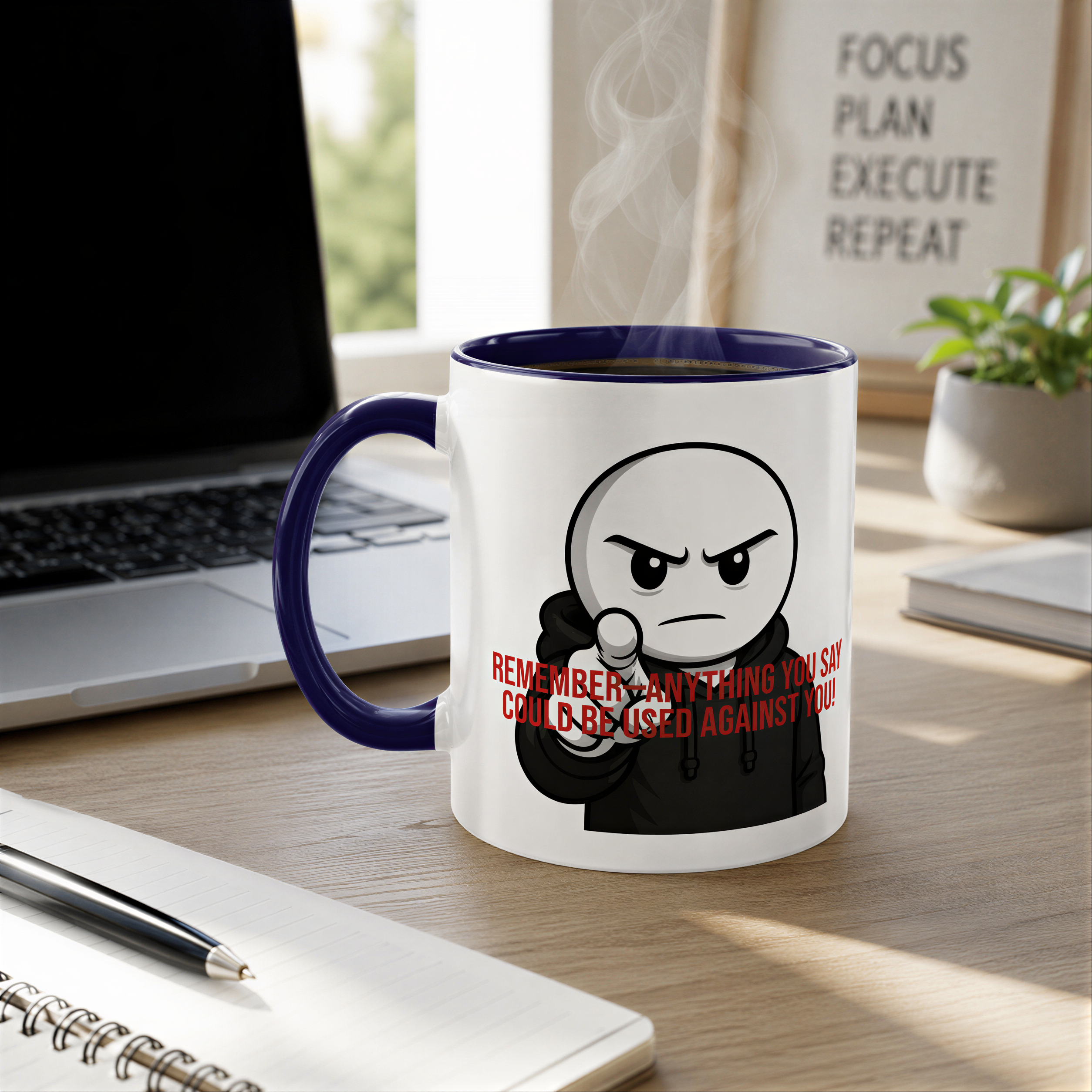 A mug with a cartoon character and text on it, placed on a wooden desk next to a laptop and a notebook.