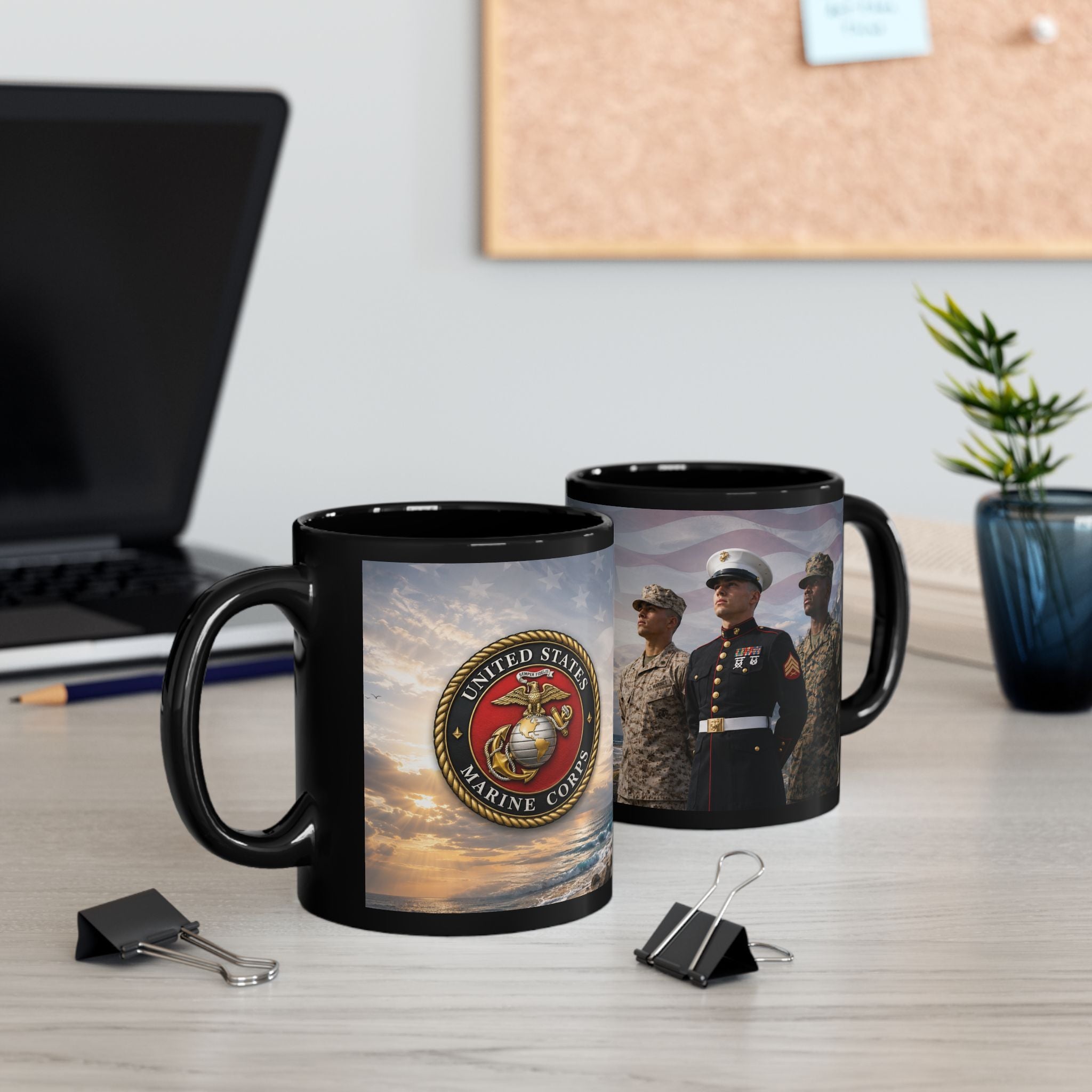 two black mugs with the United States Marine Corps logo, placed on a desk with a laptop, a plant, and some office supplies.