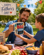 A man and a young boy are sitting at a picnic table, with the man holding a mug that says "Best Dad Ever". The table has a sandwich, a bowl of fruit, and a drink. In the background, there is a banner that says "Happy Father's Day!".