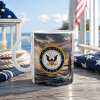 A mug with a design featuring the United States Navy seal, placed on a wooden surface with a view of the ocean and a flag in the background.