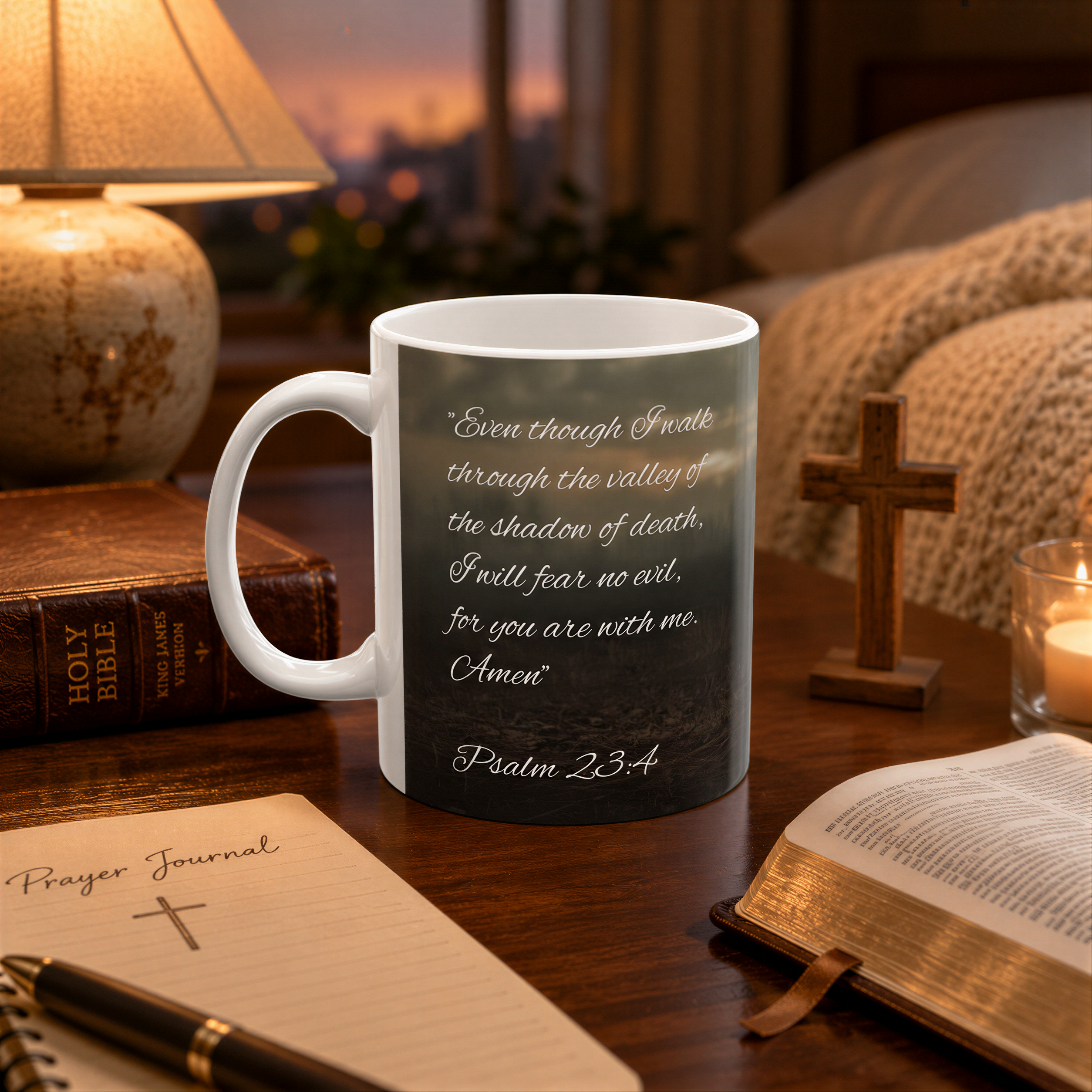 A white mug with a Bible verse printed on it, placed on a wooden table next to a notebook, a lamp, and a candle.