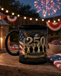 A black coffee mug with an American flag design and the text "United States of America" printed on it, along with the number "250" and "Honor + Sacrifice Liberty" printed below. The mug is placed on a wooden surface, with a bowl of berries and a string of lights visible in the background.