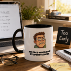 a mug with a cartoon character on it, placed on a desk with a laptop, glasses, and a notebook.