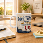 A white mug with a motivational quote sits on a wooden desk, surrounded by office supplies and a laptop.