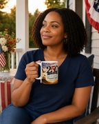 A woman with curly hair is sitting on a porch, holding a mug with a design that says "250th BULLIE COLLEGE FOUNDATION TOUCHER".